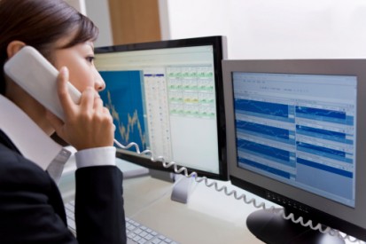 Woman on phone while viewing data on double monitors