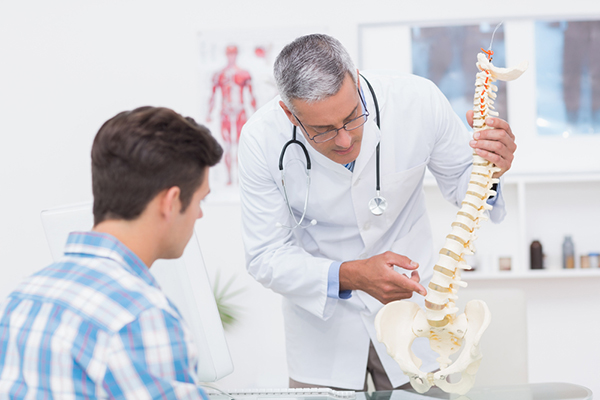 Medical professional with a patient pointing to a Vertebral Column model