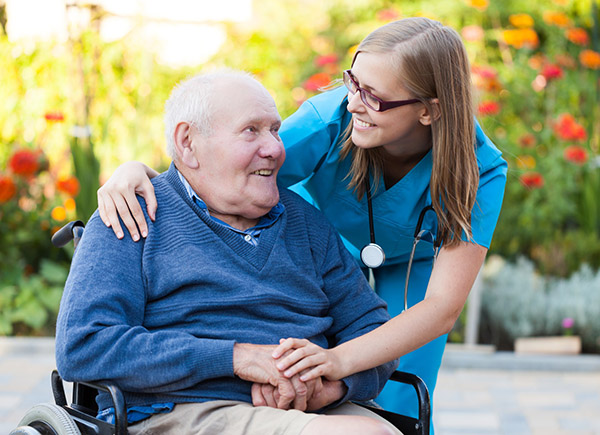 Elderly man in a wheelchair smiling with a medical professional as she speaks to him