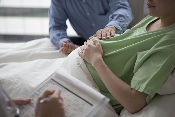 Pregnant woman in hospital bed speaking to a medical professional with a man at her side