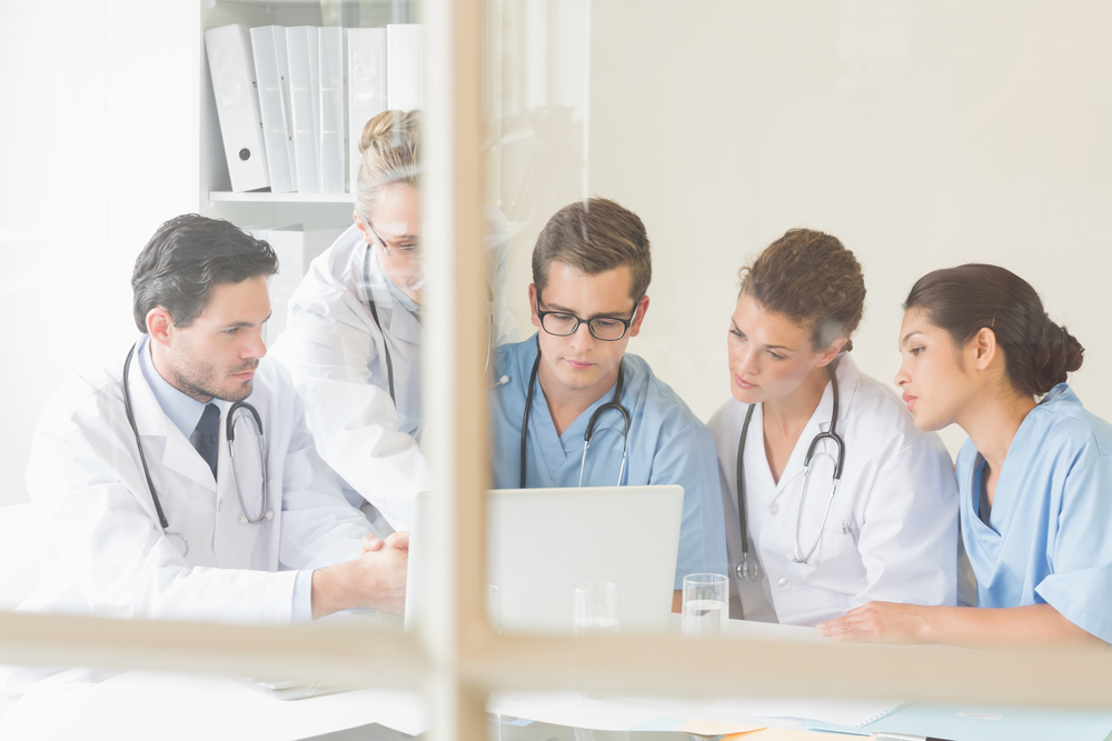 Medical professionals surround a computer deep in discussion