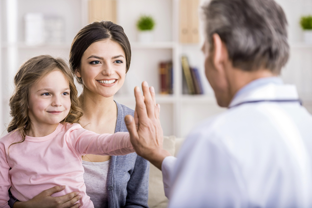 Pediatrician high-fiving a girl sitting in her mother's lap