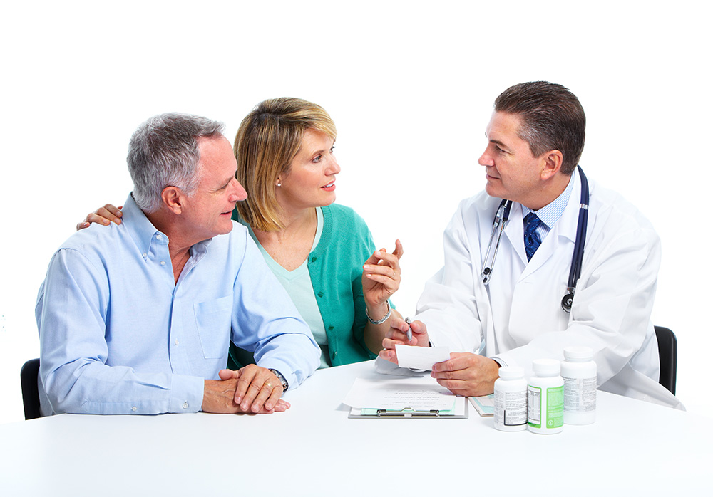Middle aged couple smiling and speaking to a medical professional with medical reports and medicine bottles on the table