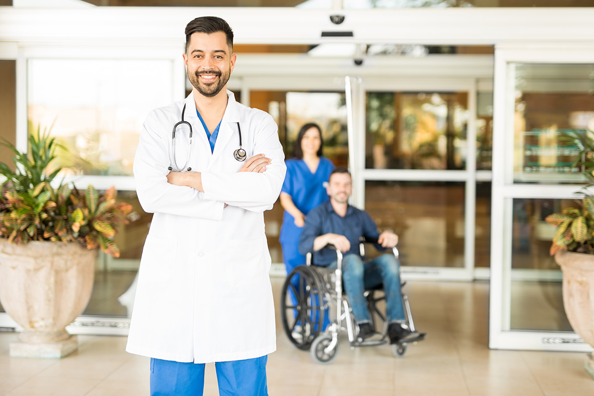 doctor smiling outside of emergency room while a patient gets wheeled out