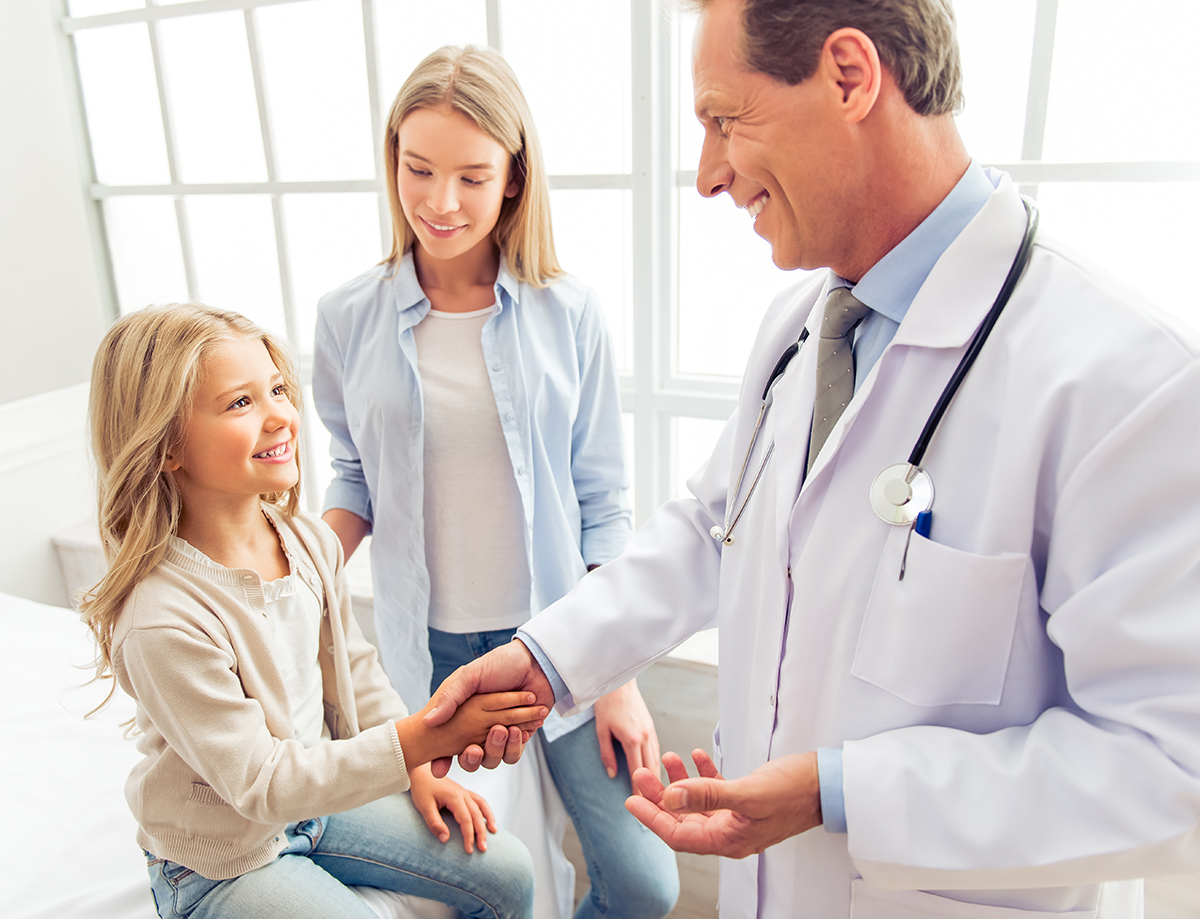 doctor shaking hands with young girl while mom watches